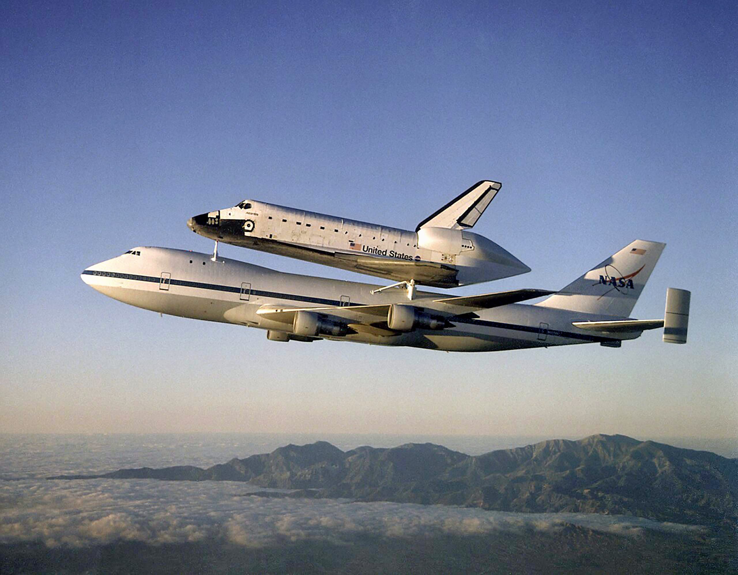 The Space Shuttle orbiter Atlantis, framed by the California mountains, as it rides on the back of one of NASA's Boeing 747 w:Shuttle Carrier Aircraft (SCA) en route from California to the Kennedy Space Center, Florida, after a ten month refurbishment. (By NASA / Carla Thomas - Armstrong Photo Gallery: Great Images in NASA: Public Domain, Wikimedia Commons)