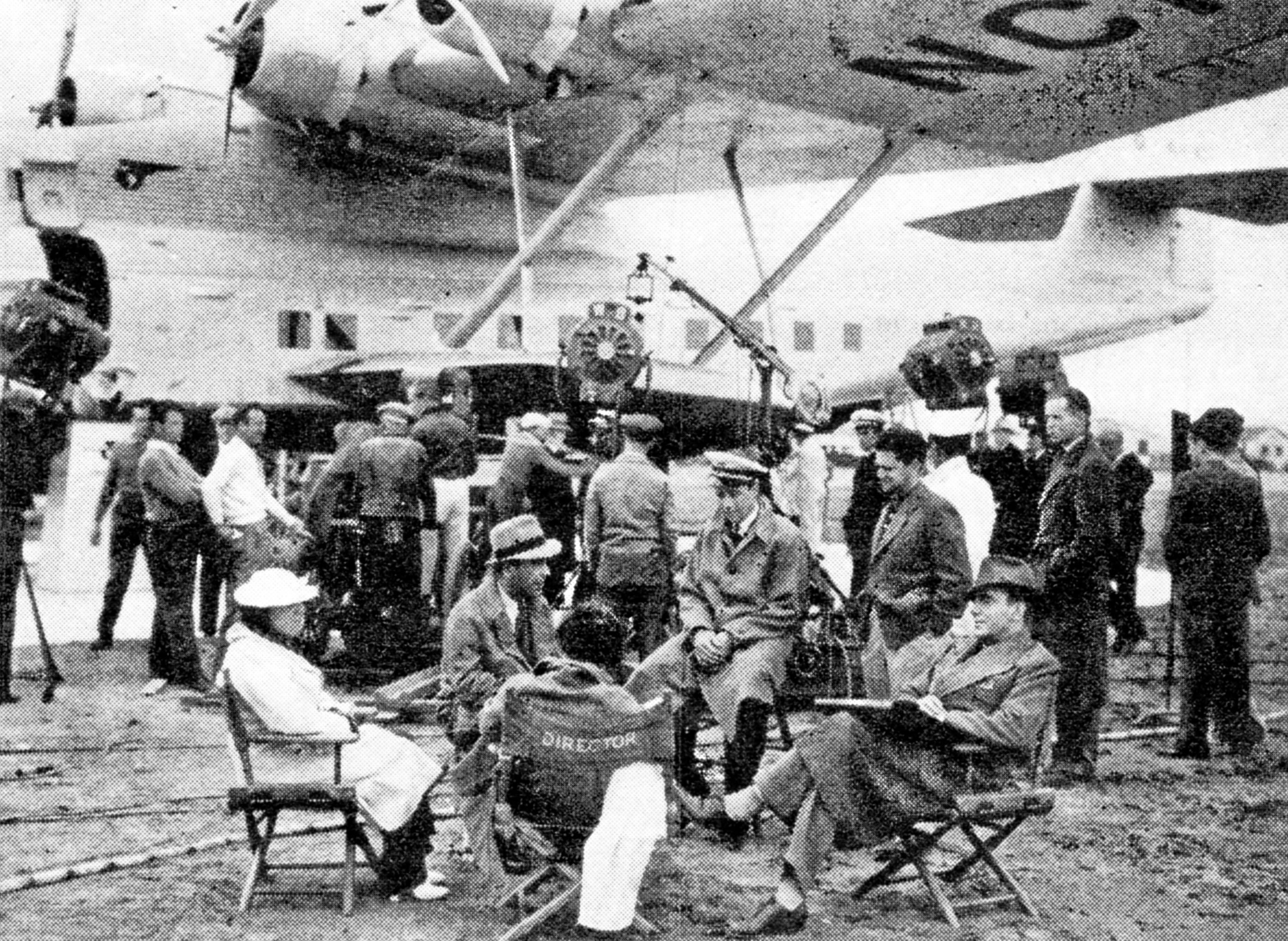 Cast and crew at Alameda, "where an 'operations' conference had to be called to solve a problem in navigating the script." (L- to-R) Foreground: Mrs. Henry B. Walthall; Humphrey Bogart; scriptgirl; Ross Alexander; Owens-chief cutter; and Pat O'Brien("Pan American Air Ways").